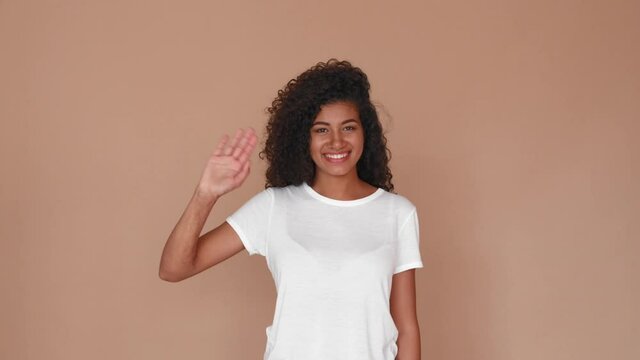black woman smiling laughing and waving hello with hand on brown studio background