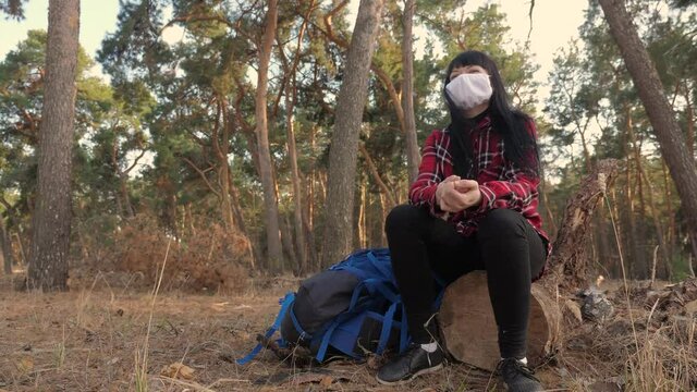 tourist hiker girl resting in the woods on a stump near a hiking backpack. concept pandemic virus lifestyle epidemic world catastrophe infection covid
