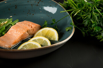 A piece of red fish, beans and lemon in a plate, next to it is a bunch of parsley