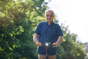 Obraz premium Senior man riding electric kick scooter in the park 