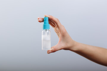 Woman's hand holding spray bottle sanitizer isolated on gray background