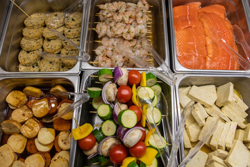 Variety of fresh skewers and meat products on the butcher display refrigerator in the Supermarket. salmon, shrimps, tofu and vegetarian patties in top view.
