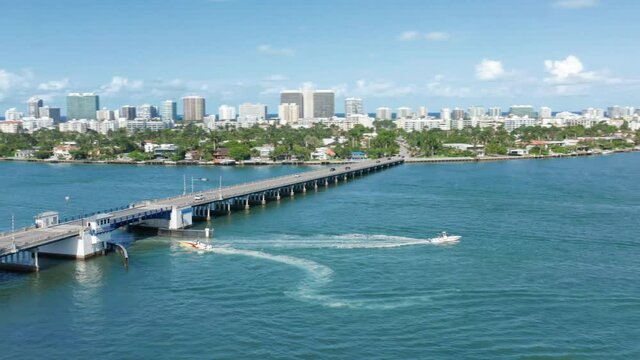 Aerial view on beautiful skyline of city at the ocean, with tropical islands in the bay on a sunny summer day. Drove flying above the bridge over blue waters of Miami harbor. 4K aerial Florida, USA