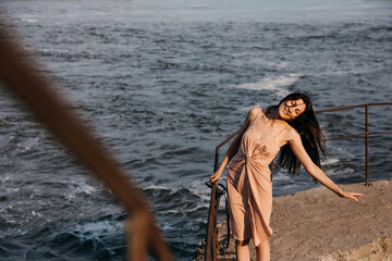 Young slim woman, wearing a summer dress, dancing and smiling on a pier by the sea.