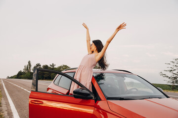 Young woman with hands up in the air out of a car. Summer road trip concept.