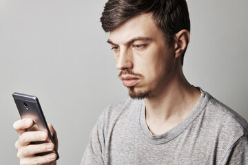 portrait of handsome guy looking at mobile phone. isolated over grey background. copy space. caucasian male person dressed casual clothes. studio shot.