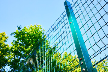 Fototapeta na wymiar green fence barrier over green trees and sky background. private security concept. sunny day. bright future concept.