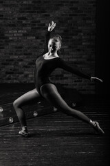Ballerina in dark bodysuit, in dress in dark interior Studio. Wall of bricks, piano.