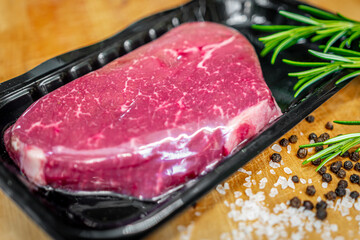 Beef steak in vacuum skin packaging and spices on wooden chopping board