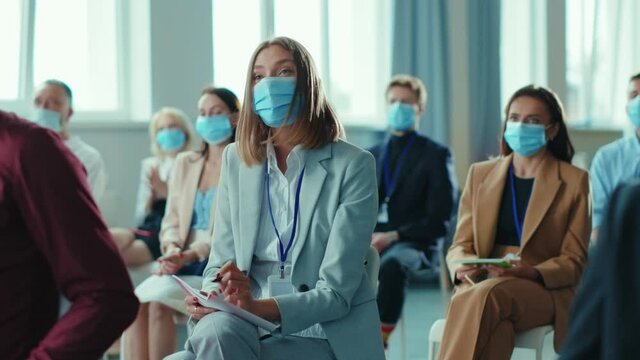 Young femle entrepreneur negotiating with speaker on business seminar. Diverse business people applauding on conference meeting wearing protective masks. Lockdown and career.
