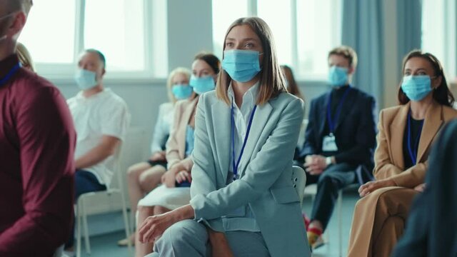 Diverse group of business persons wearing protective masks and listening to speaker lecturer at corporate seminar conference meeting. Pandemic outbreak. Workspace.