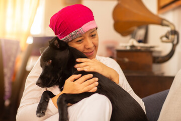 latin woman hugging her pet, woman with pink scarf on her head due to breast cancer