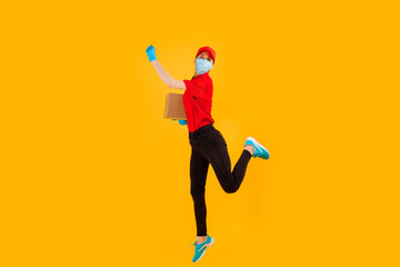 Fototapeta na wymiar A cheerful, excited, Bouncing female courier in a red Cap and t-shirt, uniform, medical protective mask and gloves, with boxes in her hands, on a yellow background. coronavirus
