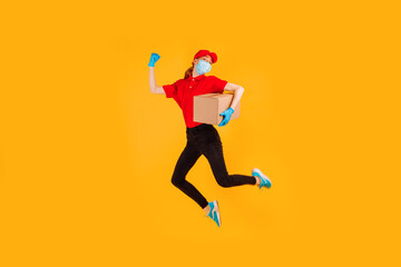 Fototapeta na wymiar A cheerful, excited, Bouncing female courier in a red Cap and t-shirt, uniform, medical protective mask and gloves, with boxes in her hands, on a yellow background. Delivery service