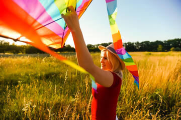 Happy young woman running with a kite on a glade at sunset in summer