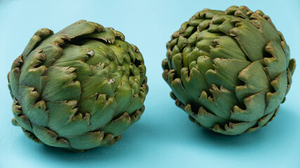 Obraz premium Two fresh green artichokes on an aqua blue background