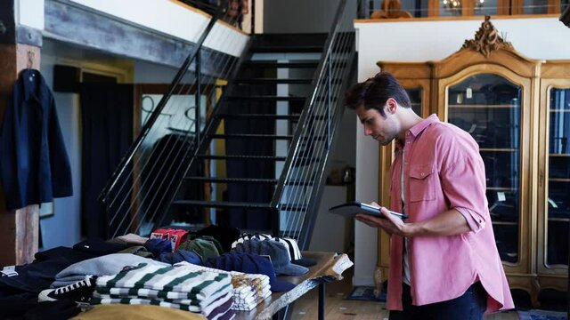 Male Owner Of Fashion Store Using Digital Tablet To Check Stock In Clothing Store