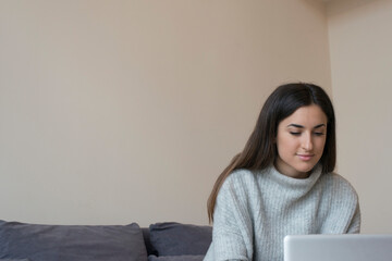 Young Brunette woman working on a laptop on a grey couch and white background