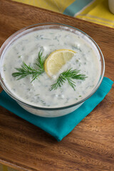 Tzatziki. Traditional Greek or Turkish homemade dip. Made with Greek yogurt, cucumbers, lemon juice, olive oil and dill. Served with mini rainbow carrots & crispy pita chips on a wooden cutting board