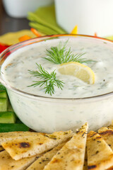 Tzatziki. Traditional Greek or Turkish homemade dip. Made with Greek yogurt, cucumbers, lemon juice, olive oil and dill. Served with mini rainbow carrots & crispy pita chips on a wooden cutting board
