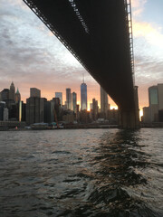 Passing under the Brooklyn Bridge on the East River at sunset, Manhattan skyline at sunset.  Setting sun, bright sunset against New York City skyscrapers. New York City skyline, sunset from East River