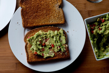 Avocado Toast. Classic American Diner Breakfast or Brunch Restaurant menu item: avocado toast. Made w/ fresh avocados smashed into guacamole and chopped tomatoes with salt and pepper served on toast.