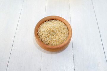  A bowl filled with uncooked white rice. On top of a white wood table   
