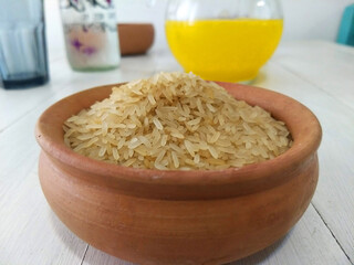  A bowl filled with uncooked white rice. On top of a white wood table   
