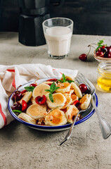 Trendy home breakfast with tiny pancakes, honey and cherries on a concrete table.