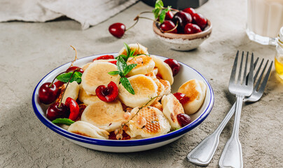 Trendy home breakfast with tiny pancakes, honey and cherries on a concrete table.
