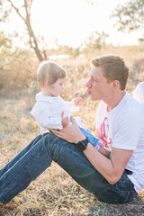 A young red-haired man holds a small beautiful daughter in his arms. She rolls it on her shoulders, plays, shakes, carries on hands. The baby laughs in her two teeth. Parenthood concept, child care