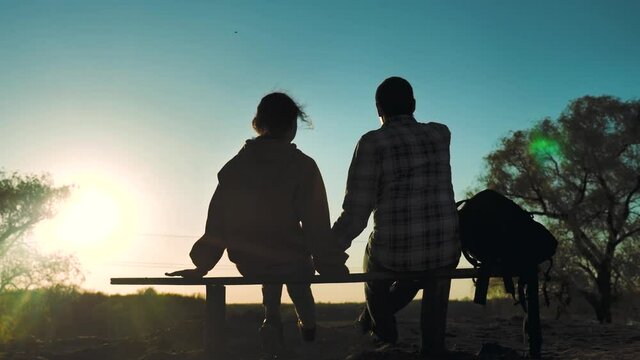 happy family man and girl teamwork sitting on a bench silhouette sunset in the park and nature. dad and daughter relax in the park spend together. couple in love hold lifestyle hand sit back look at