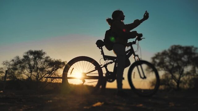 teenage girl photographs herself on a smartphone with a bicycle rides in the park at sunset on nature. healthy girls and bike makes lifestyle selfie