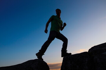 silhouette of a young man stepping over a gorge