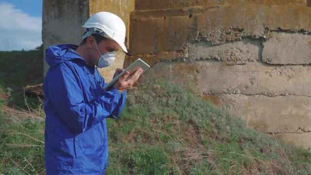 environmental pollution. man chemist scientist in a respirator mask studies landfill dump pollution radioactive waste disposal digital tablet and an white helmet stands next to standing radiation