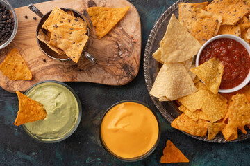 Different potato and pita chips, assorted with salsa and various dip on a dark green background