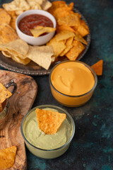 Different potato and pita chips, assorted with salsa and various dip on a dark green background