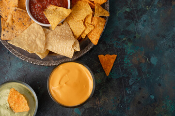 Different potato and pita chips, assorted with salsa and various dip on a dark green background