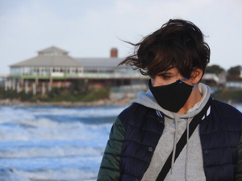 Niño con tapaboca paseando por la playa en un día frió en tiempos de pandemia