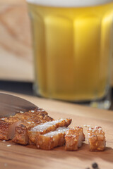 Chinese roasted pork belly cut into slices on a wooden cutting board., with a glass of beer