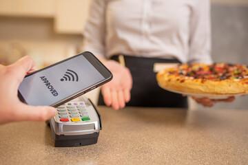 Payment by contactless payment for pizza in a restaurant or cafe, cashless payments, banking services. A new life according to the rules for coronavirus