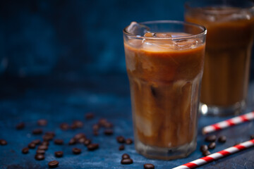 Cold cool summer drink, coffee with ice and milk on a background of a blue wall with coffee grains