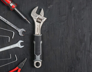 Wrenches and screwdrivers lie on the left on a black background and with place for text on the right, close-up top view.