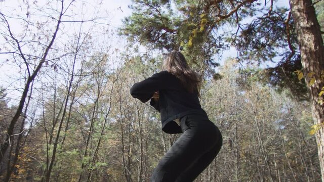 Healthy long-haired female in black clothes having physical drill outdoors doing squats looking at morning sun. Low angle 4K 360 degree tracking arc shot.