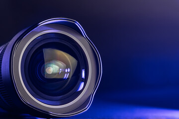 The camera lens with blue light. Close-up of the camera lens on a black background with blue illumination. Optics.