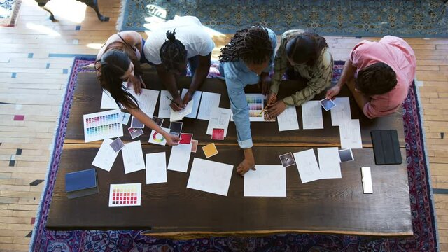 Overhead View Of Team Having Creative Design Meeting Around Wooden Table In Office