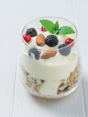 A glass of yogurt, granola, berries and almonds on a white table.