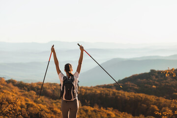 Woman happy to hike top of mountain and hold trekking poles. Nordic walking outdoors, view from behind. Travel lifestyle. Success goal achievement. - obrazy, fototapety, plakaty