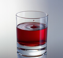 Drop of wine fly up above the surface in glass. Red wine glass close up.