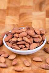 Almonds in white ceramic bowl on wooden table.